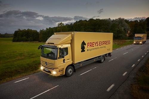 En mångfaldig grupp människor som sitter och står runt ett bord på ett kontor och diskuterar flytt med ett starkt ljus som kommer från bakgrunden.